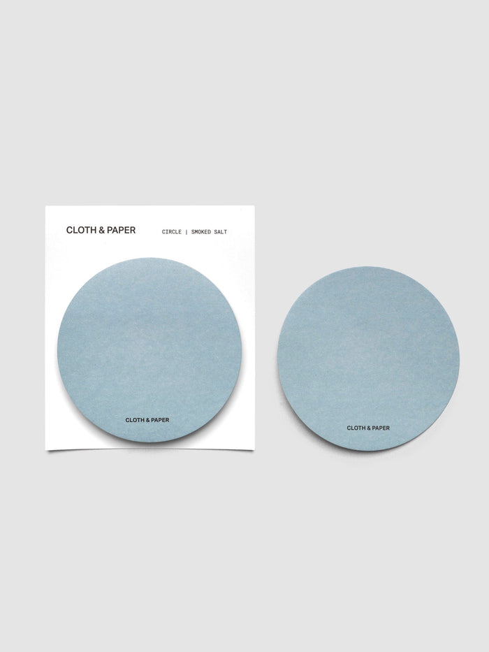 A stack of light blue circular sticky notes on a white backer card with one note peeled off and placed beside it