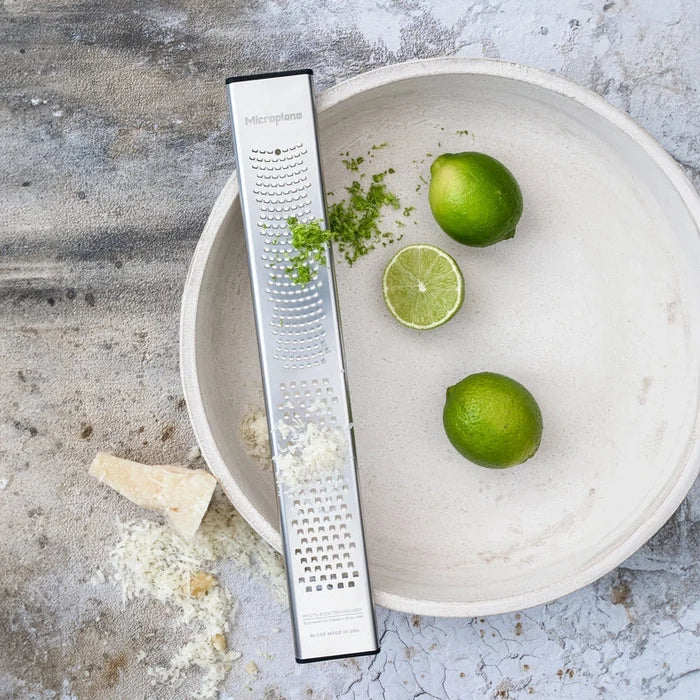 Zester next to a bowl with limes on a textured surface