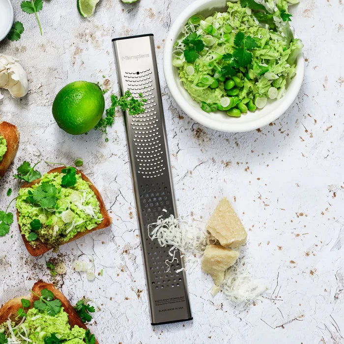 Avocado spread on toast with a bowl of guacamole, lime, and cheese on a textured surface.