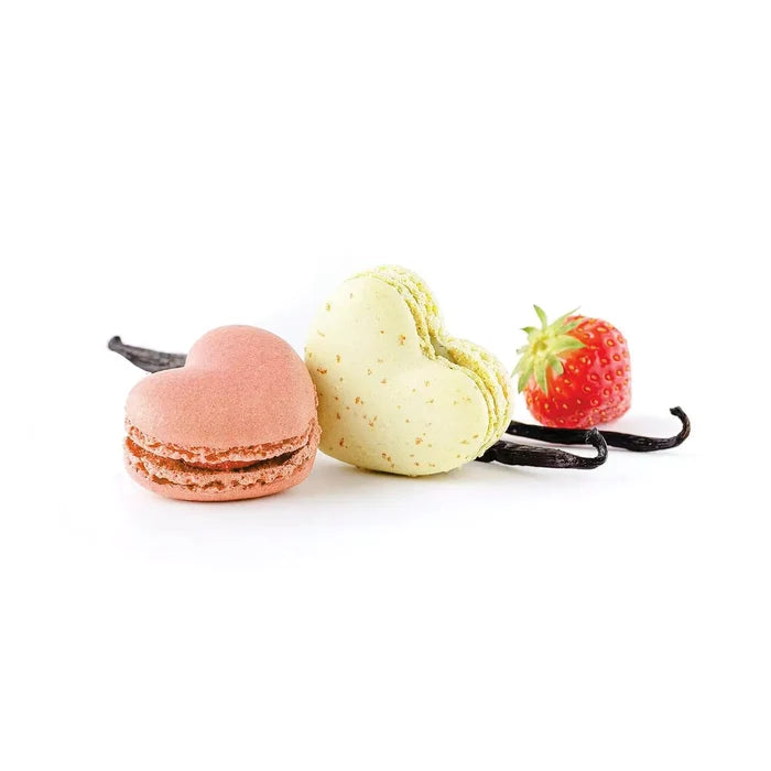 Two heart-shaped macarons with a strawberry and vanilla bean on a white background