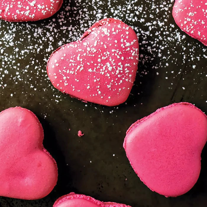 Heart-shaped pink macarons with powdered sugar on a dark surface