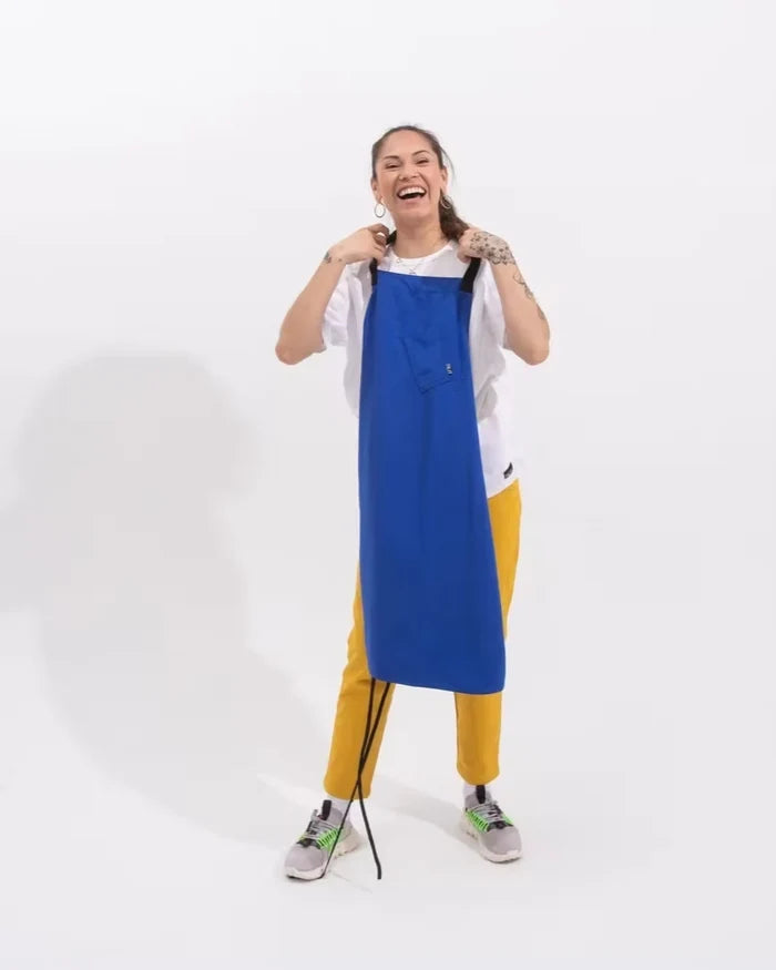 Person wearing a royal blue apron over a white shirt with yellow pants on a white background